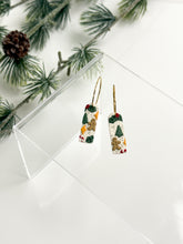 Load image into Gallery viewer, Christmas-themed earrings on a white surface with greenery in the background
