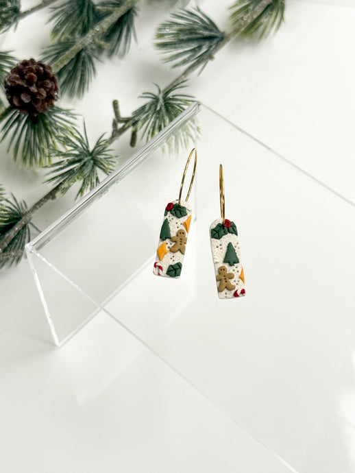 Christmas-themed earrings on a white surface with greenery in the background